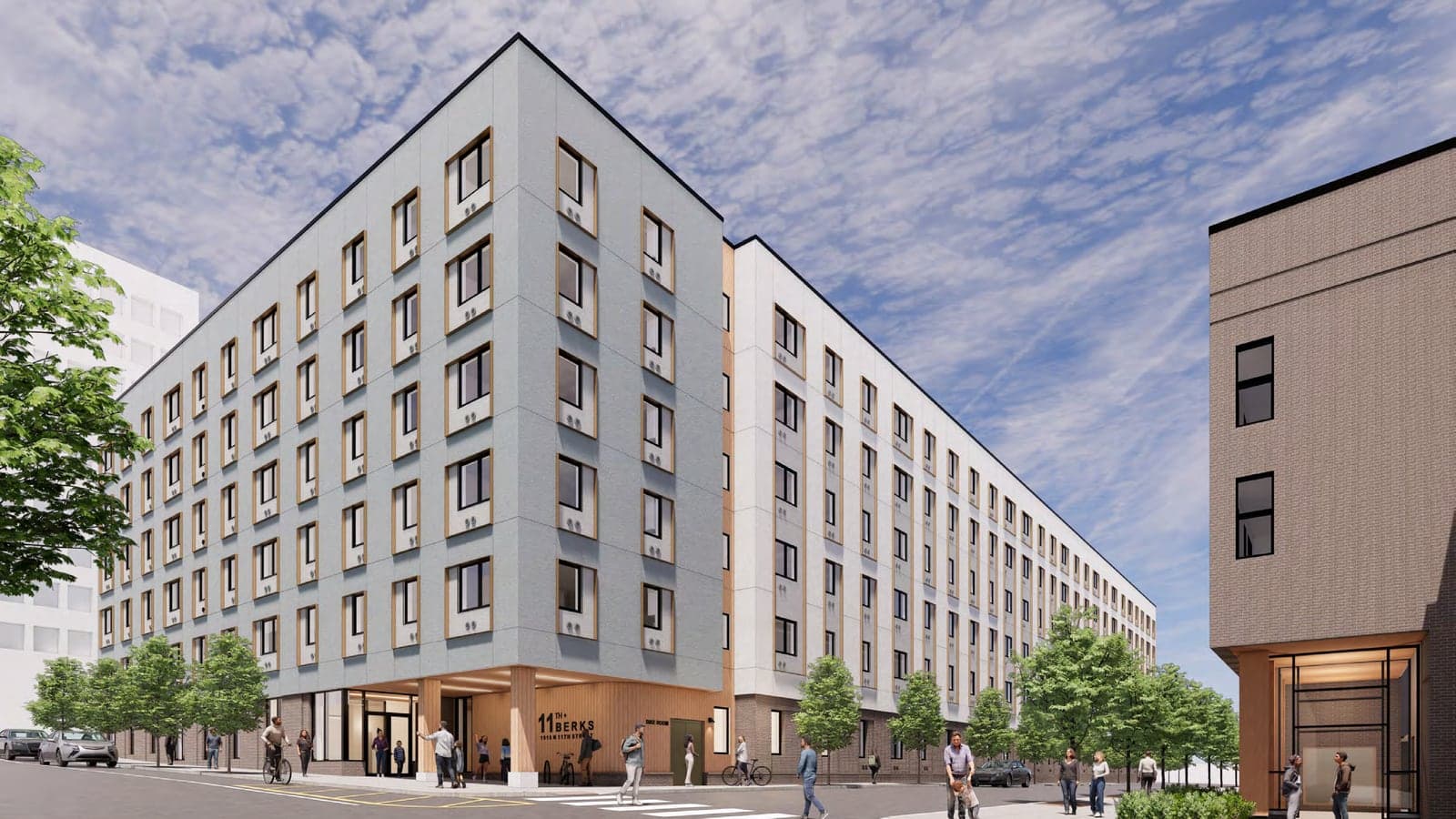 Rendering of a six-story apartment building in gray and white panels with wood-toned window surrounds, a recessed corner entrance marked 11th and Berks, street trees and people on the sidewalk