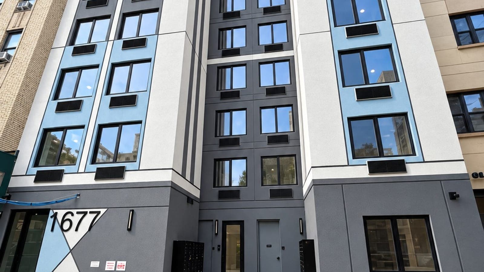 Lower floors of a new apartment building with white, grey and light blue panels, dark window frames and the number 1677 beside the entrance
