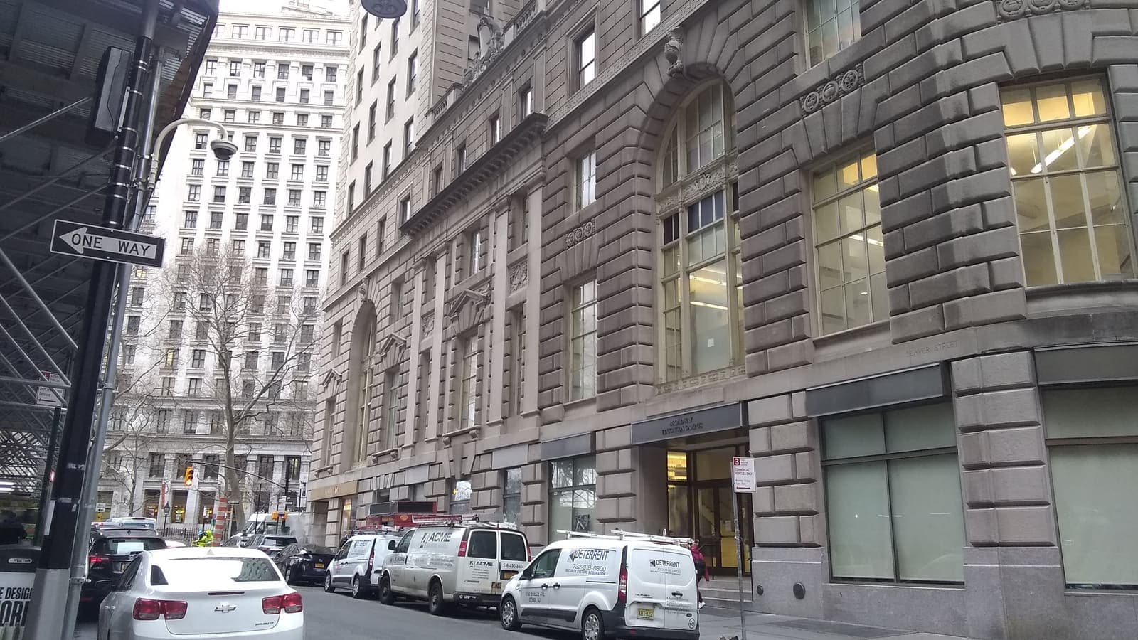 Stone office buildings lining a narrow street, with vans parked at the curb and a tall white office building at the far end.