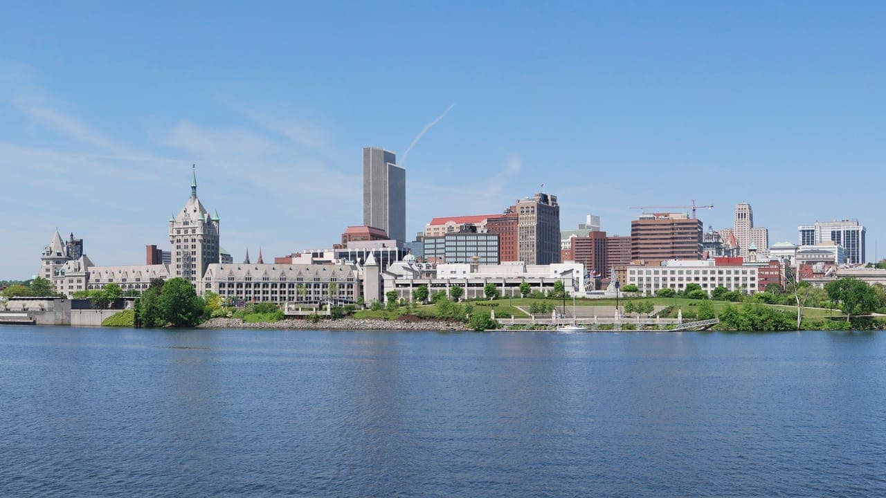 Albany's skyline, with the turreted state university building at the left and the tall Corning Tower behind it, seen across the Hudson River