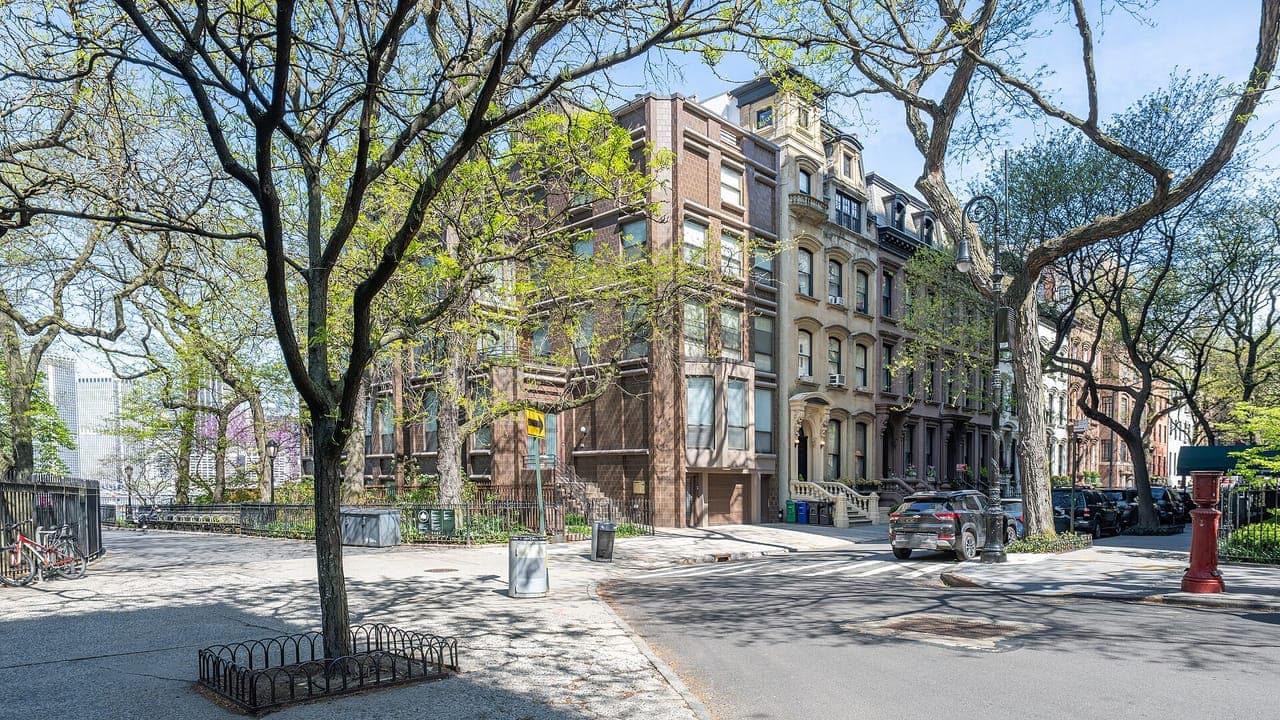 Brownstone and brick rowhouses at a corner of a tree-lined street in Brooklyn Heights on a sunny spring day