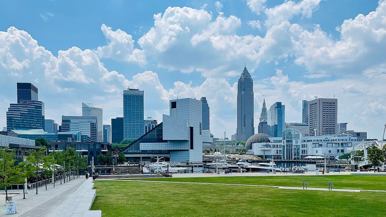 Downtown Cleveland's skyline, with Key Tower and the glass Rock and Roll Hall of Fame, seen across the lawn of a lakefront park