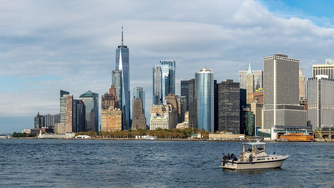 Lower Manhattan's towers, with One World Trade Center the tallest, seen across the harbor with a small fishing boat in the foreground