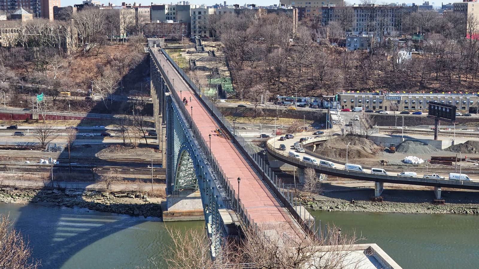 Photograph from above of the High Bridge, a long arched bridge with a red-brick walkway crossing a green river, with highways, rail tracks, bare trees and apartment buildings on the far bank