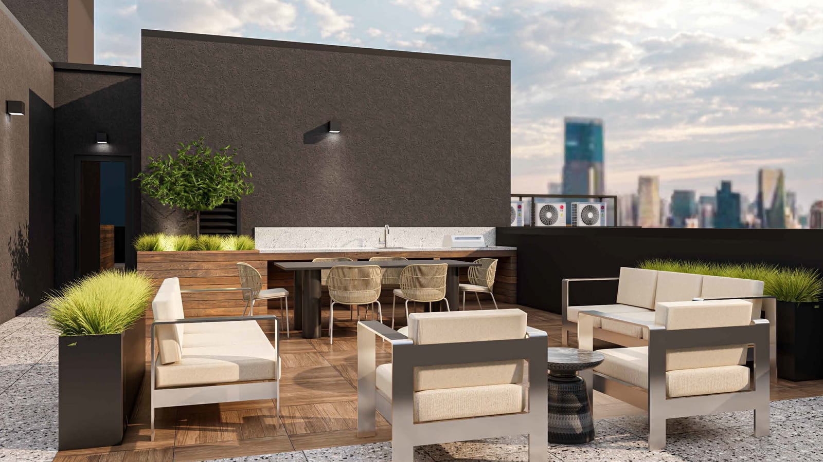 Rendering of a roof terrace with speckled stone pavers, a wood deck, white cushioned outdoor sofas and chairs, a dining table with woven chairs, a counter with a sink and grill against a dark wall, tall planters with grasses, and city towers in the distance
