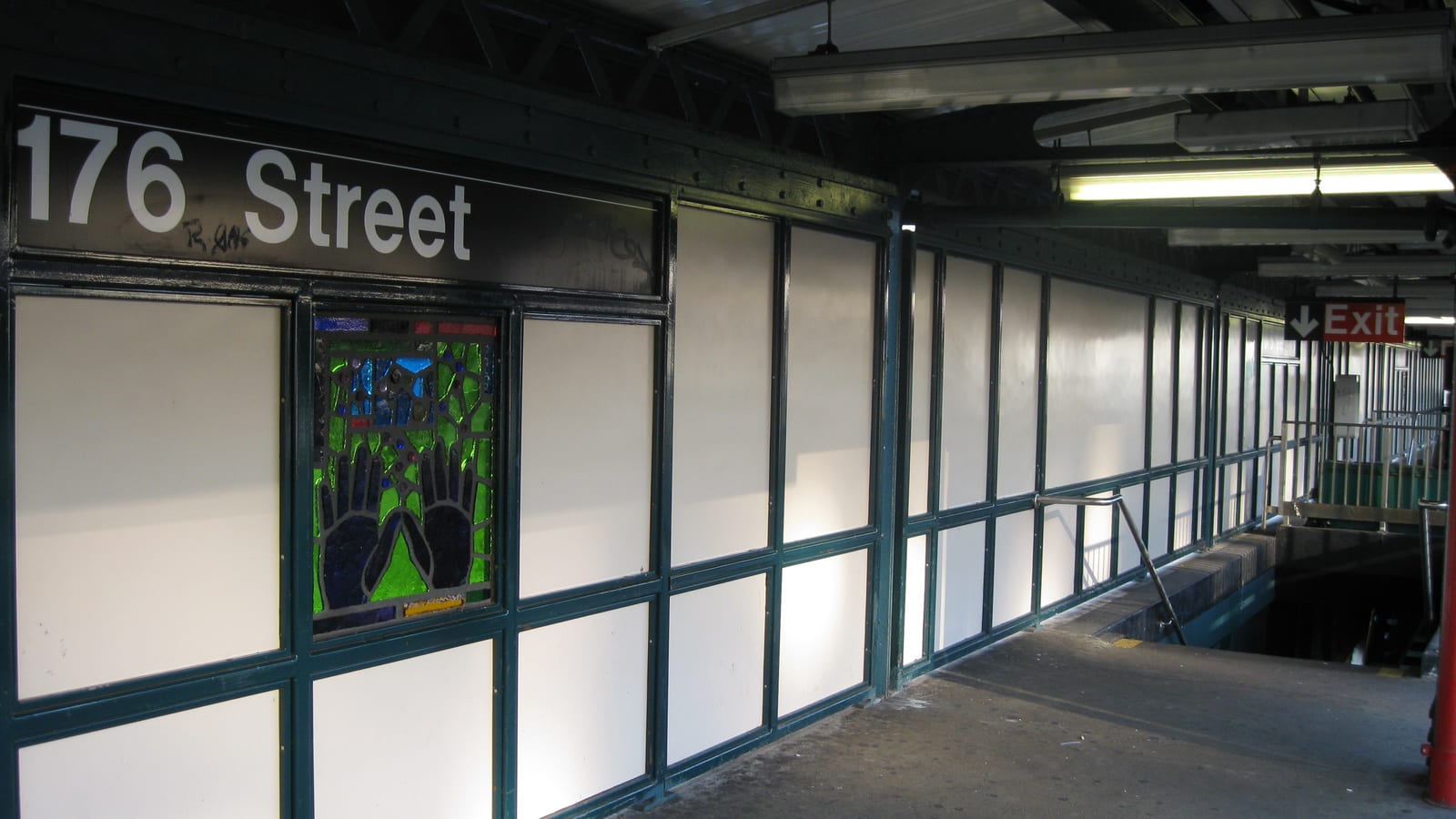 Photograph of an elevated subway platform with a black sign reading 176 Street, green-framed white wall panels, a stained-glass panel showing two hands, a red Exit sign and a stair going down