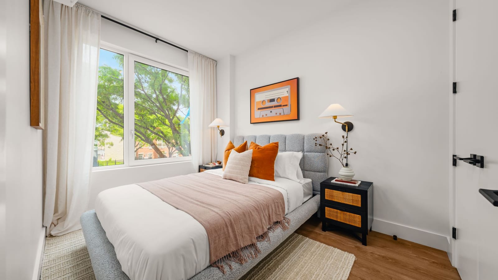 Bedroom with a made bed, a nightstand, framed art and a large window looking onto trees