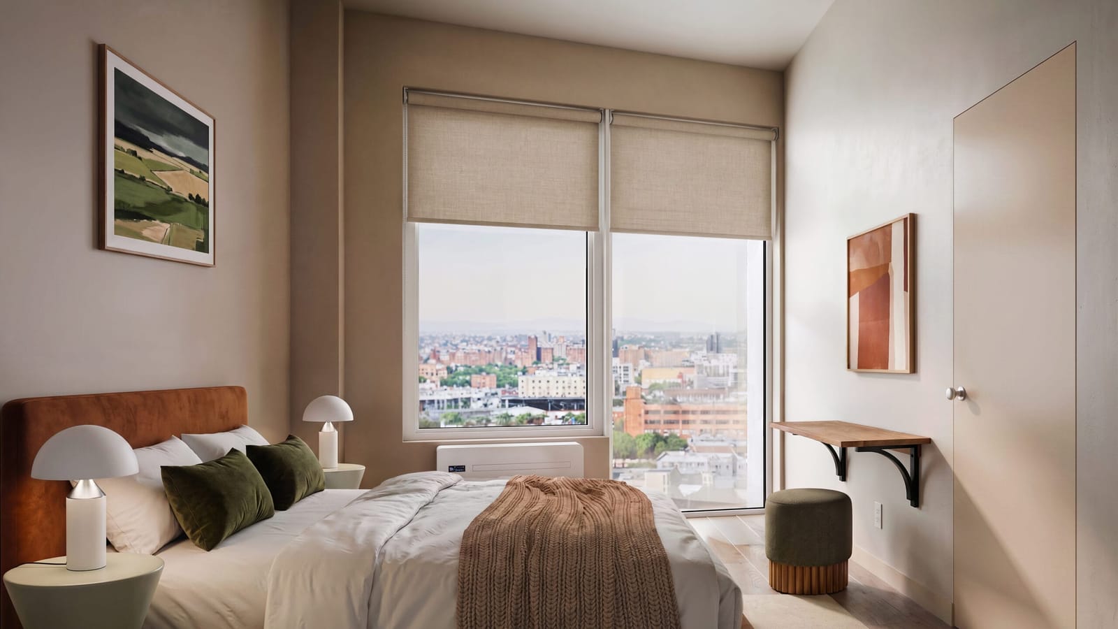 Rendering of a bedroom with a bed and rust-colored headboard, two white table lamps, a large window with linen roller shades looking out over low brick buildings, a white wall unit below the window, a small wall-mounted desk and a door at the right