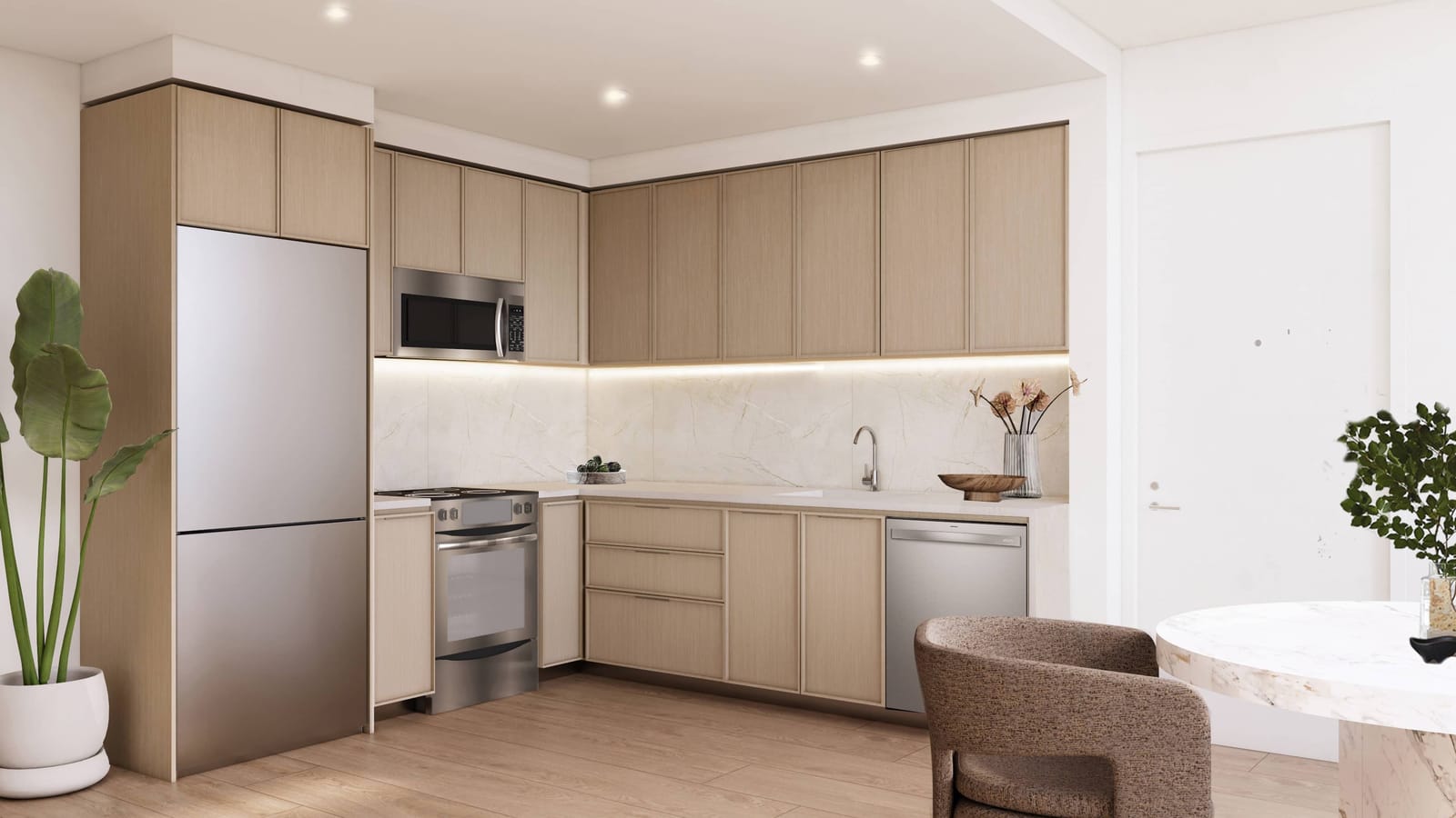 Rendering of an L-shaped kitchen with pale wood cabinets, a stone-look backsplash with under-cabinet lighting, a stainless-steel refrigerator, a microwave above a smooth-top electric range, a dishwasher and a sink, with a round marble table and a chair in the foreground