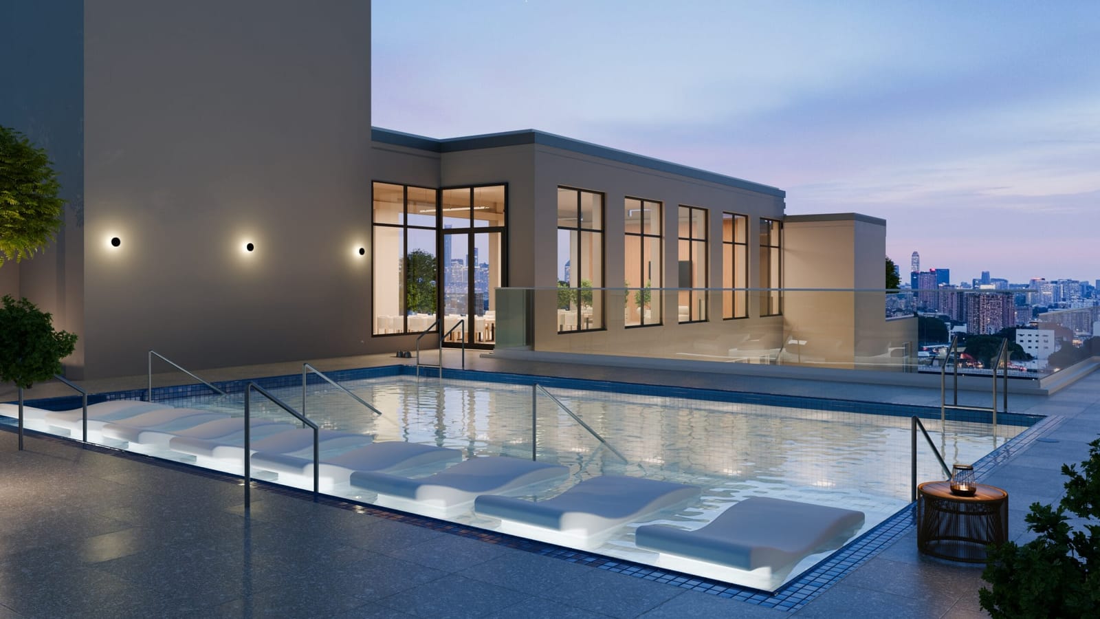 Rendering of a rooftop swimming pool at dusk with built-in lounge ledges along one side, steel handrails, a paved deck, a glass railing and a lit glass-walled room behind it, with a city skyline in the distance