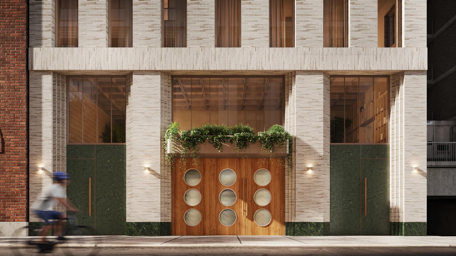 Rendering of the base of the building: pale grey brick piers, a wide wooden double door with nine round frosted windows under a planter box with trailing greenery, tall windows into a double-height lobby, dark green stone panels with brass pulls on either side, wall lights, and a blurred cyclist passing at left