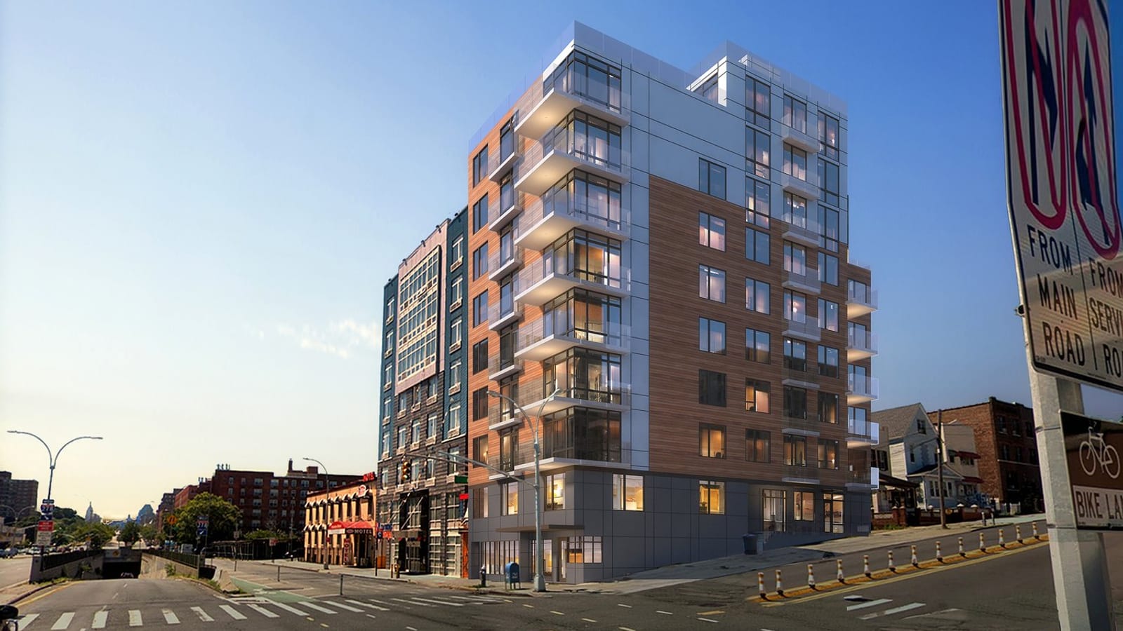 Rendering of a nine-story apartment building on a street corner under a blue sky, faced in silver metal panels and reddish woodgrain panels, with a stack of glass-railed balconies on the narrow front, smaller balconies along the long side, lit windows, and a dark grey ground floor with glass doors; a taller dark building stands to the left, a wide road with a crosswalk runs in front, and a no-turn sign reading From Main Road and a bike lane sign stand at the right edge