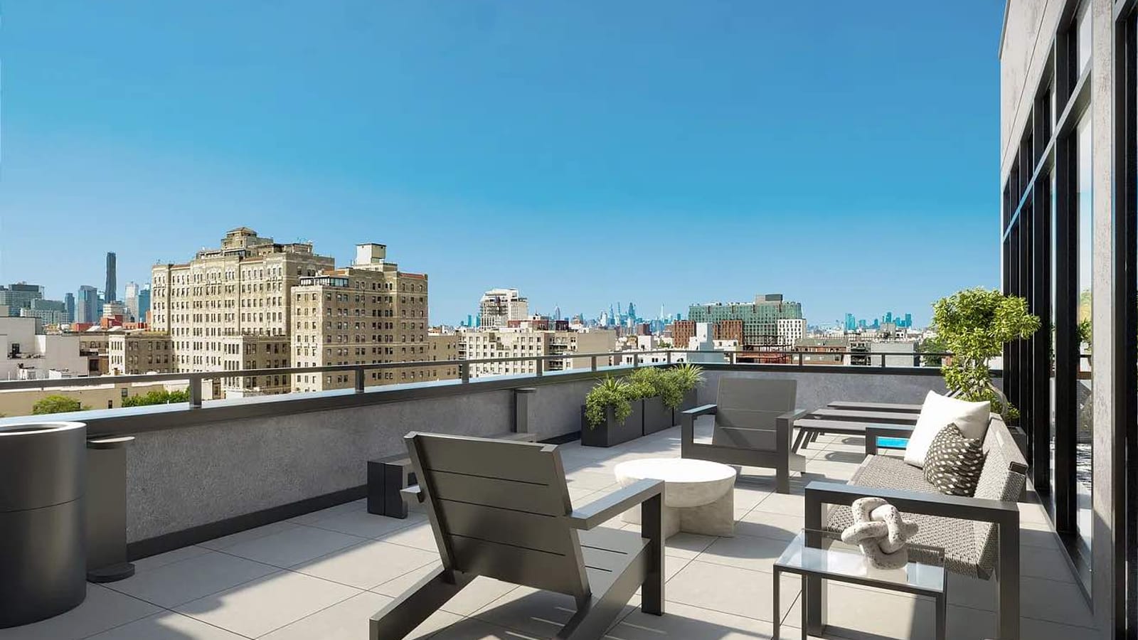 Rendering of a rooftop terrace with gray lounge chairs, a woven sofa and planters behind a railing, with tall brick apartment buildings and a distant skyline under a clear sky
