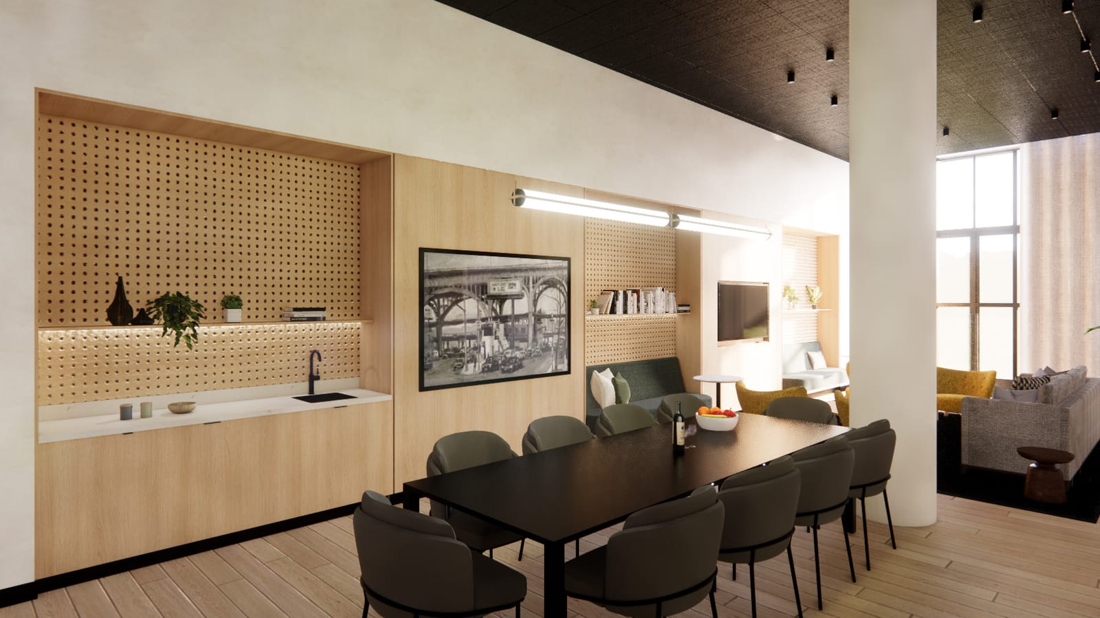 Rendering of a shared room with a long black dining table and eight dark gray chairs, a kitchenette counter with a sink under pegboard shelving, a framed black-and-white photograph of an elevated bridge, and a lounge area with a wall screen beyond a white column