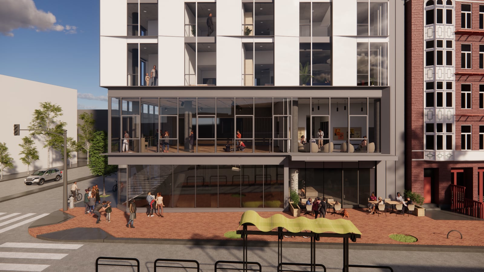 Rendering of the lower floors on a brick-paved sidewalk: a two-story glass arts space with people inside above a street-level room, cafe tables outside, bike racks and a transit shelter in the foreground