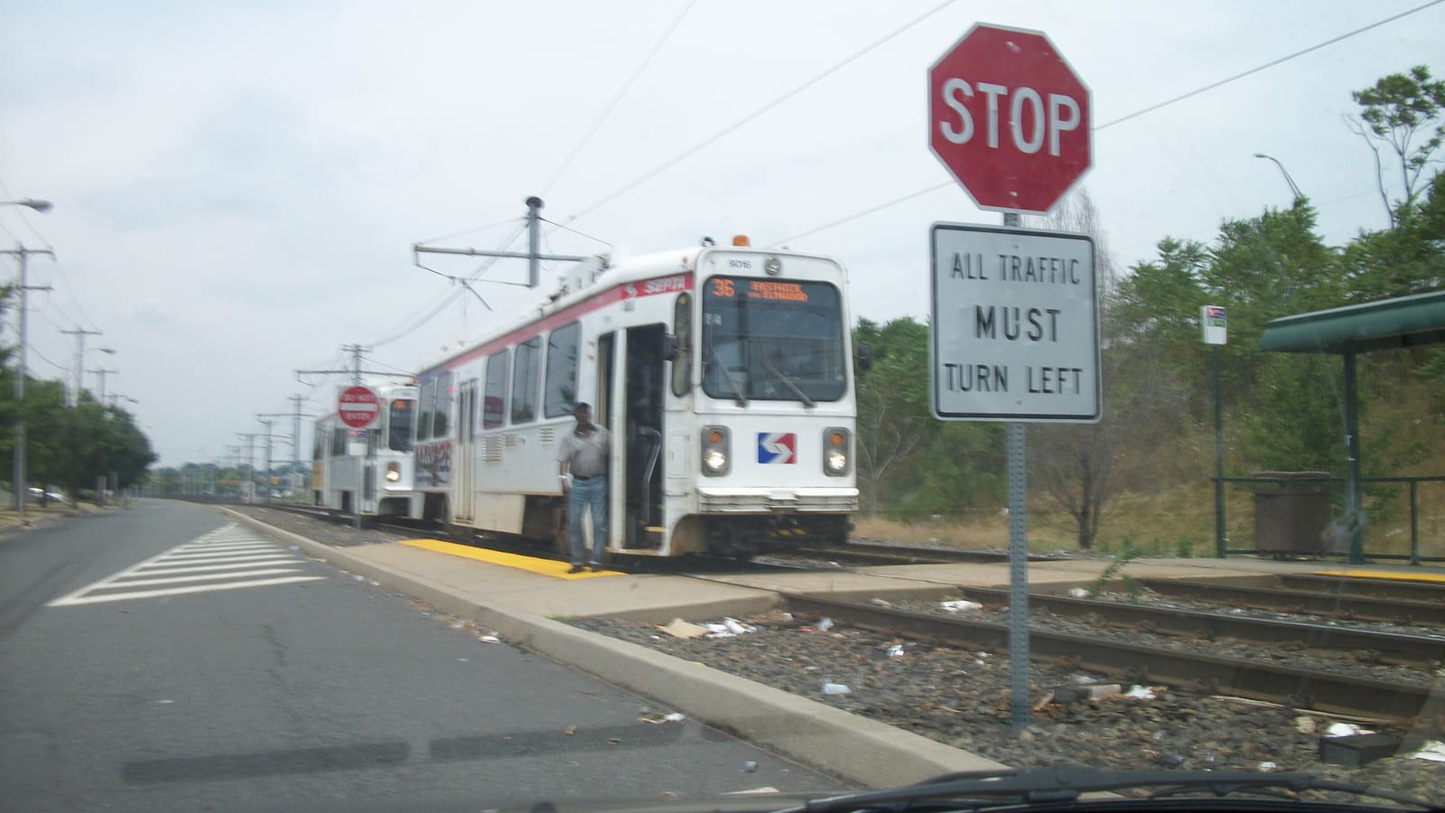 Two white SEPTA trolleys with red and blue stripes at a low platform, one showing the route number 36, beside a stop sign and a small shelter
