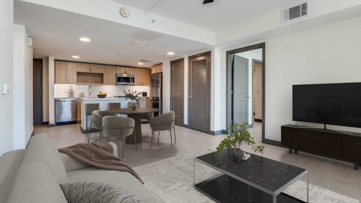Open living and dining room with a sofa, a round dining table, a wall-mounted television and a kitchen along the back wall