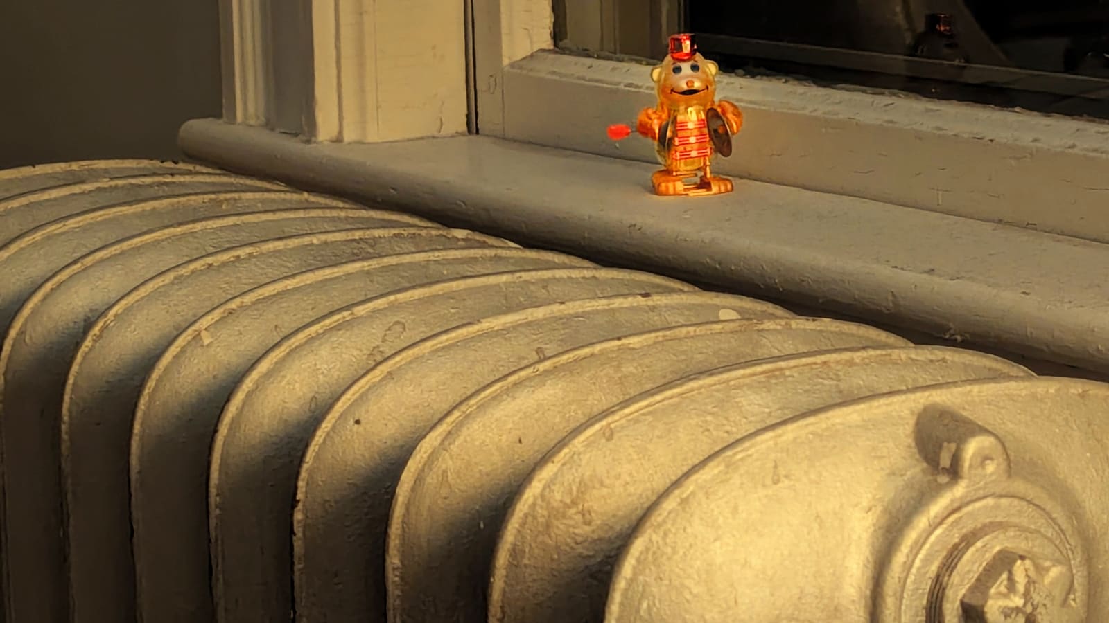 A painted cast-iron radiator beneath a window sill, with a small wind-up toy on the sill
