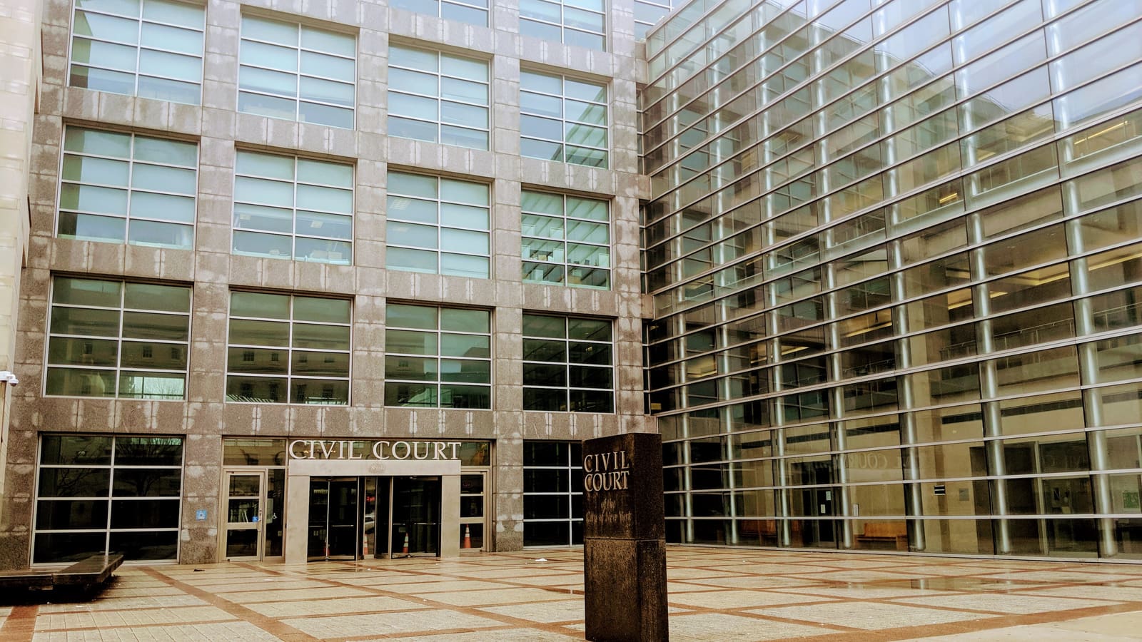 Stone and glass courthouse with Civil Court lettered over the entrance and on a stone marker in an empty paved plaza