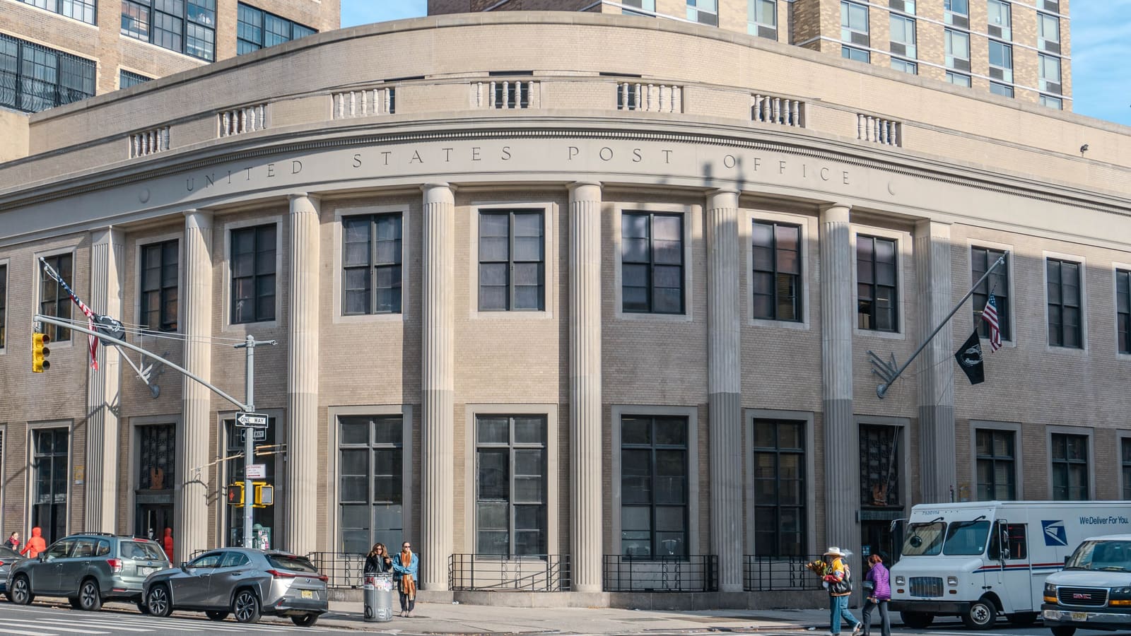 Curved brick and stone post office building with columns and the words United States Post Office carved across the front, a postal truck parked at the curb