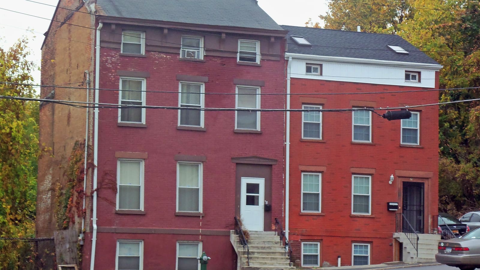 Two attached red brick rowhouses, two and a half stories tall, with stone stoops and a car parked in front