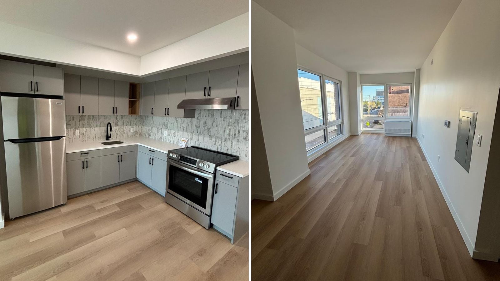 Two photographs side by side: at the left an empty L-shaped kitchen with flat grey cabinets, black handles, a white counter, a marble-pattern tile backsplash, a stainless-steel refrigerator, a smooth-top electric range and a range hood on light wood-look plank flooring; at the right an empty long living room with white walls, the same flooring, large windows on two walls, a white unit under the far window and an electrical panel on the right wall