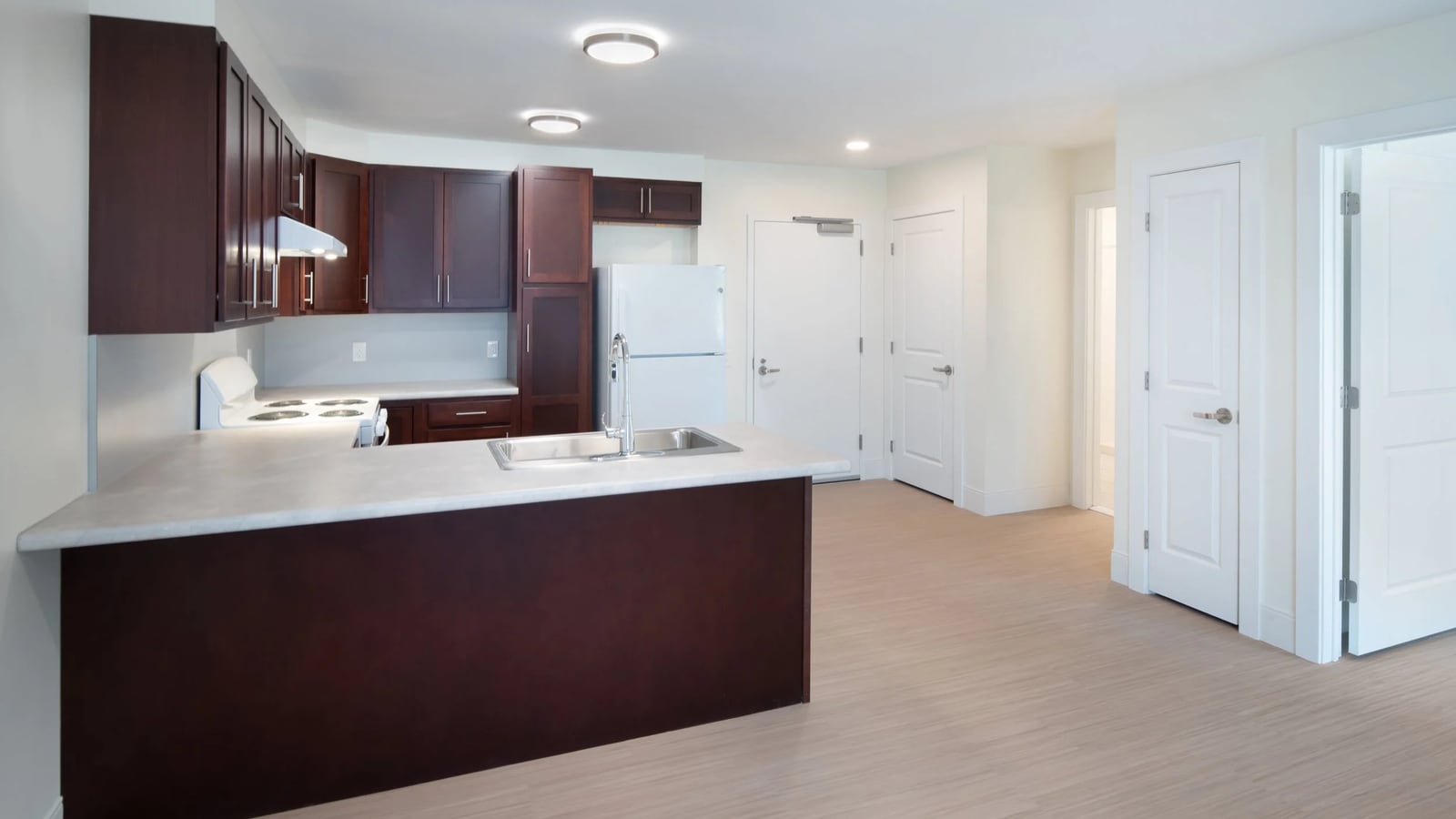 Kitchen with dark wood cabinets, a light countertop, a white electric coil range under a range hood, a white refrigerator and a steel sink