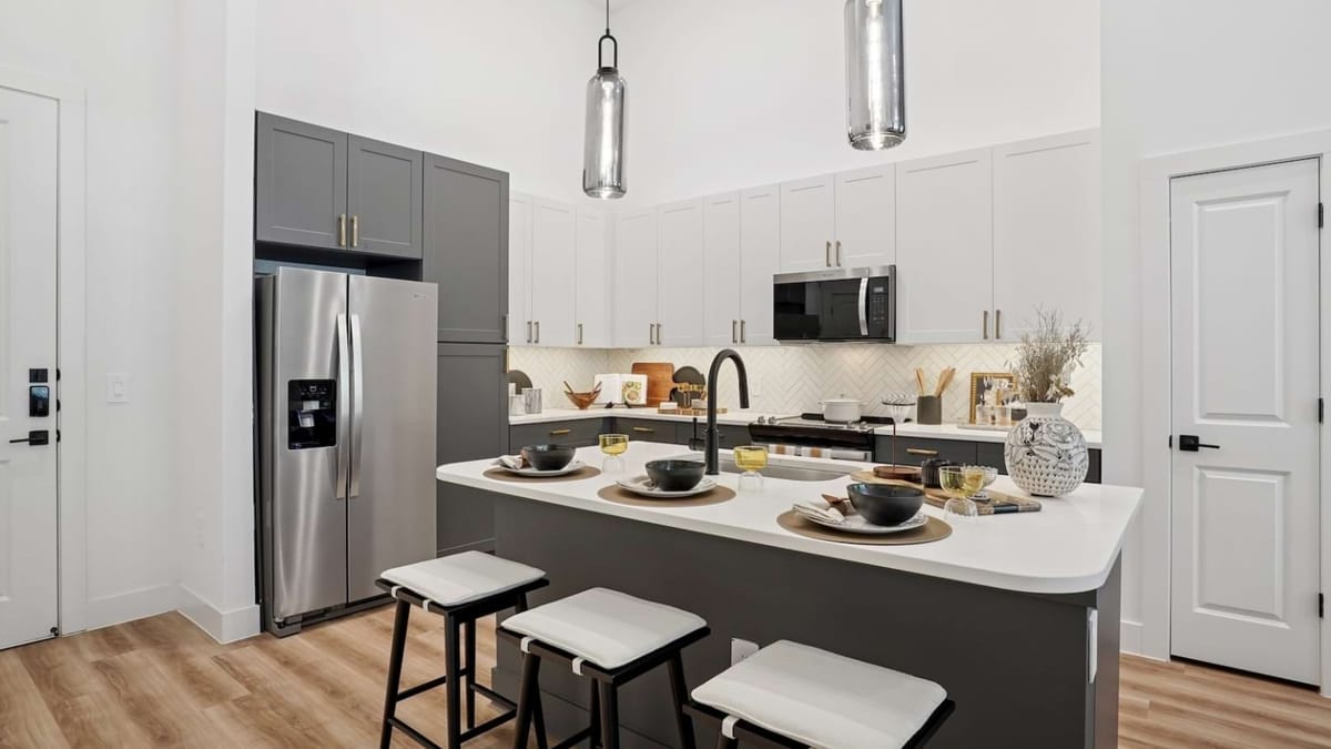 Kitchen with white upper cabinets, gray lower cabinets, a stainless steel refrigerator and a curved island set with four place settings and three stools