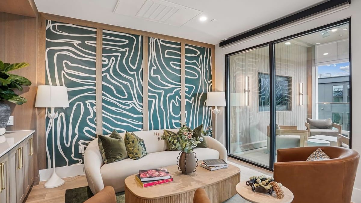 Lounge with a curved cream sofa, a round wooden coffee table and wall panels painted in a green and white pattern, beside a glass-walled room