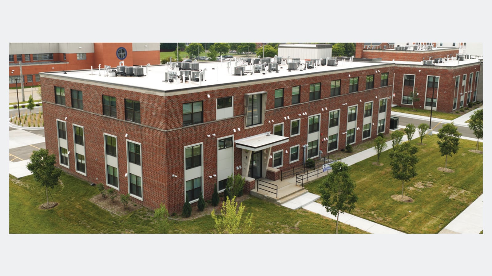 Aerial photograph of a three-story red brick building with rows of tall windows and a covered entrance, with young trees and lawn around it