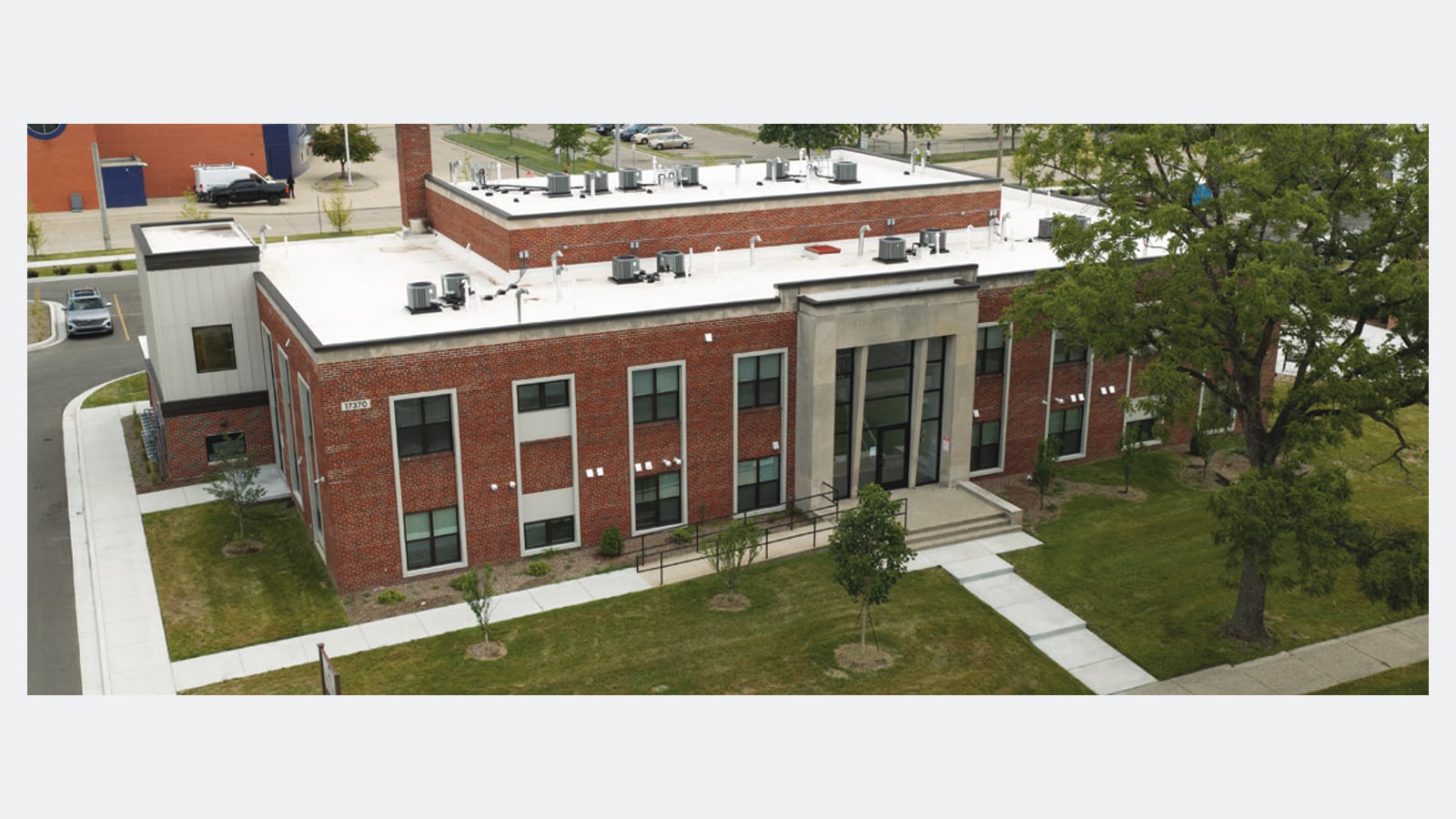 Aerial photograph of a two-story red brick building with a tall stone entrance, a flat roof with equipment and a large tree beside it