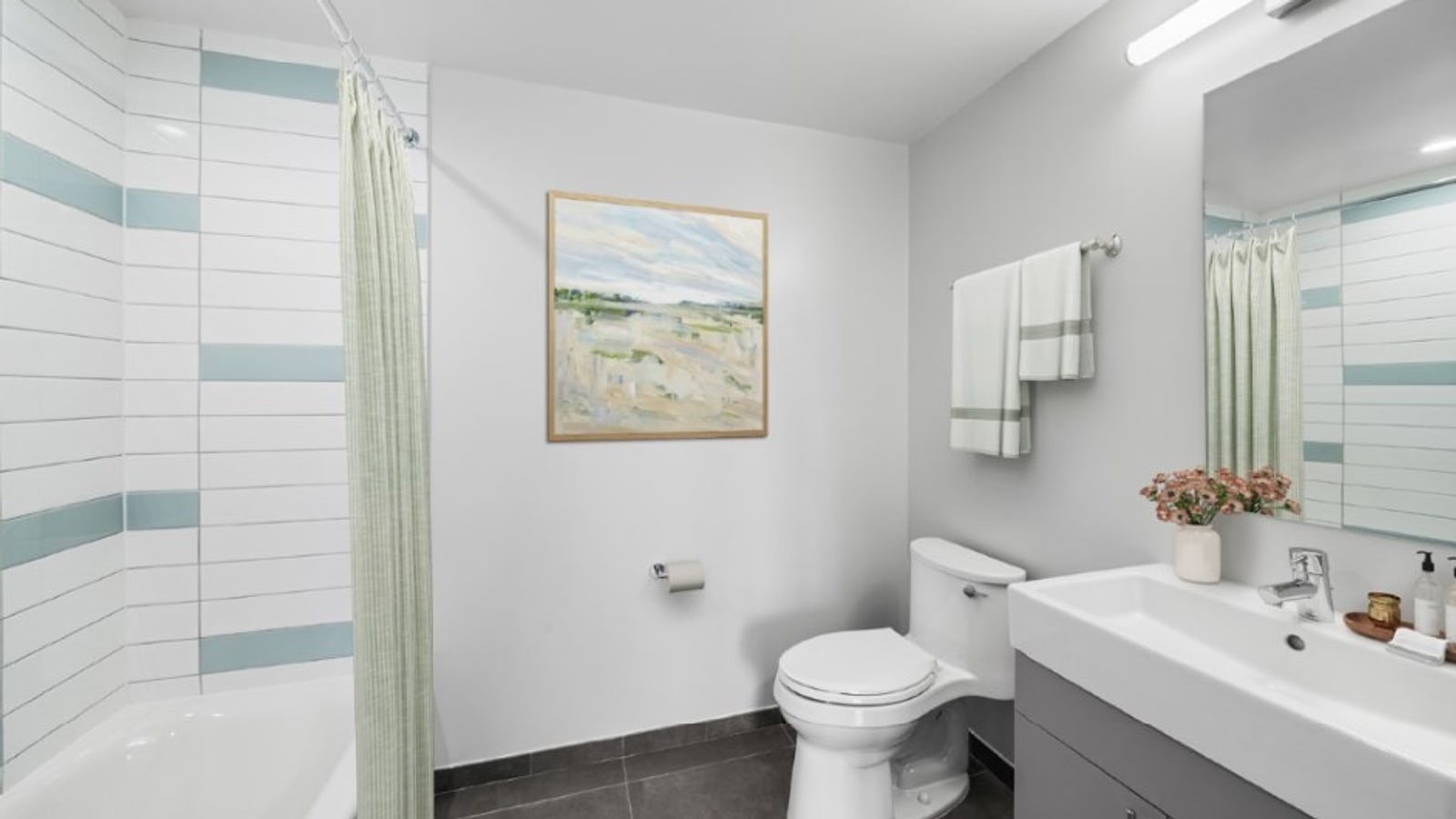 Virtual rendering of a bathroom with white and pale blue wall tile around a bathtub, a green striped shower curtain, a white toilet, a grey vanity with a rectangular sink, a mirror and dark floor tile