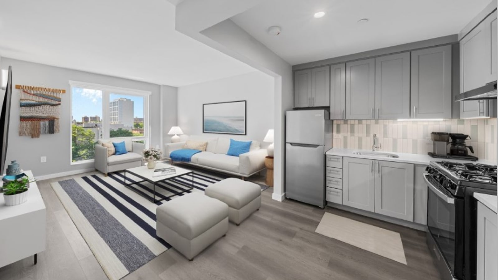 Virtual rendering of a living room and open kitchen with grey cabinets, a stainless-steel refrigerator, a tile backsplash, a black range with burner grates, grey plank flooring, white sofas on a striped rug and a window with a view of trees and buildings