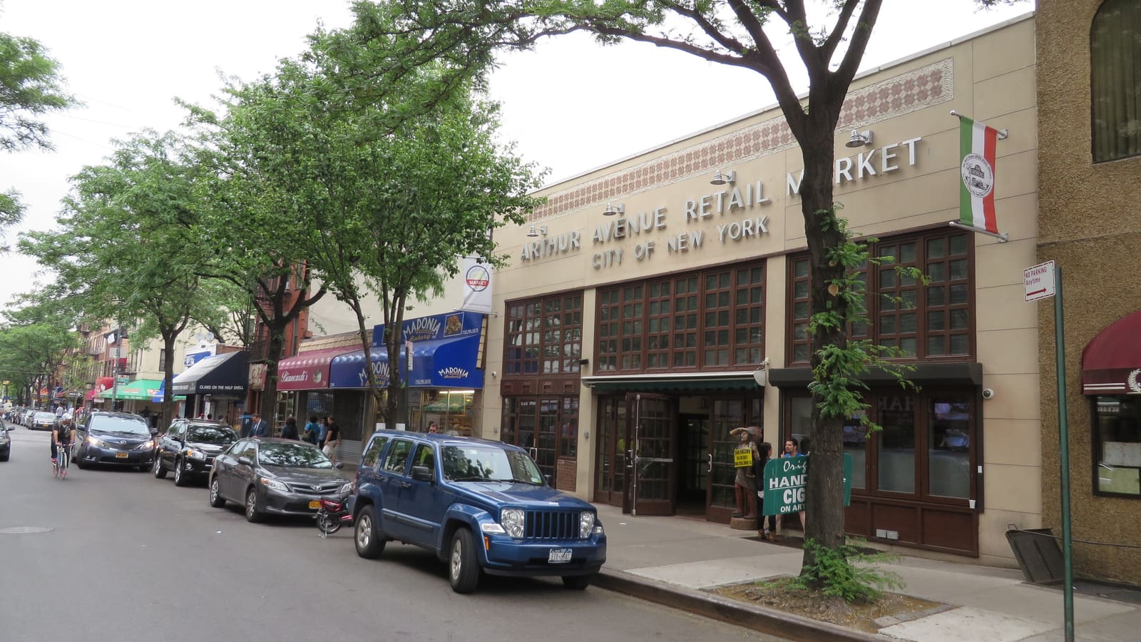 The two-storey Arthur Avenue Retail Market building with shopfronts and parked cars along Arthur Avenue