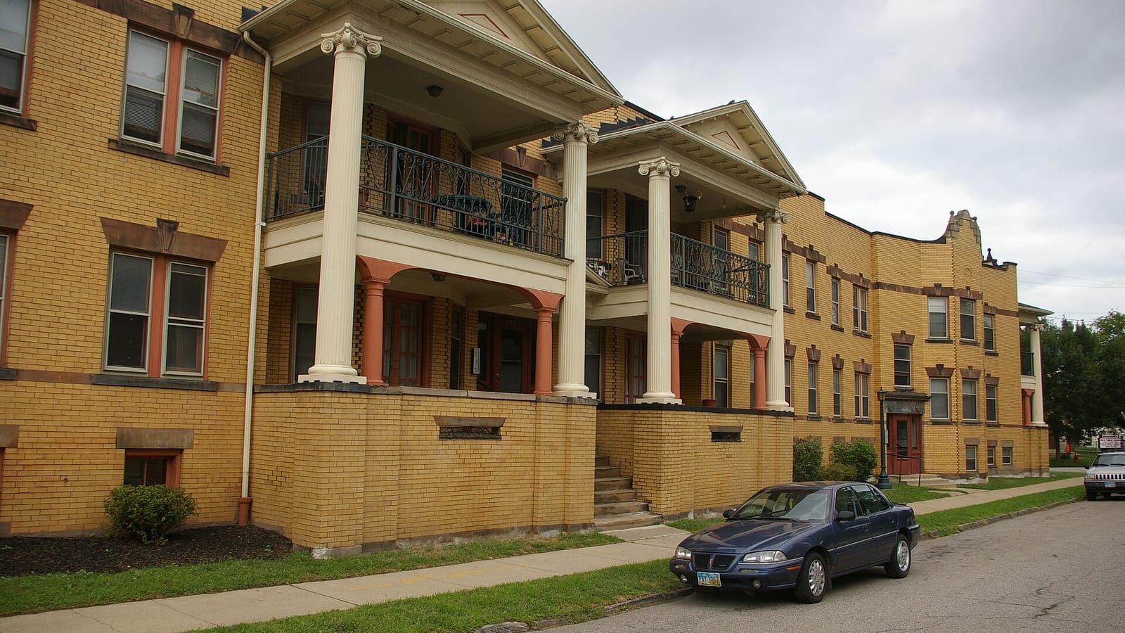 Yellow brick apartments with stacked columned porches beside a sidewalk