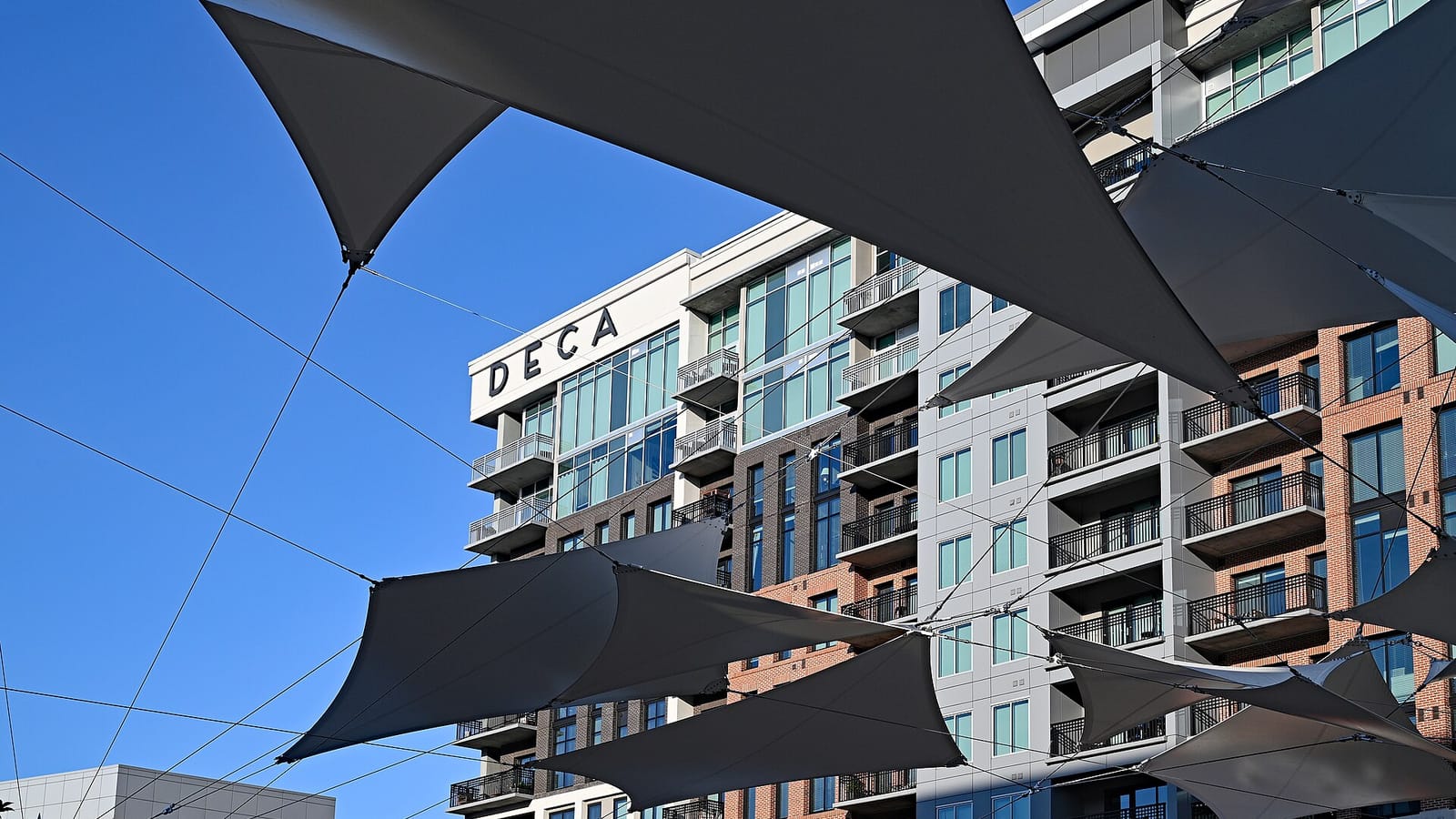 Modern apartment facade with balconies seen beyond triangular shade sails