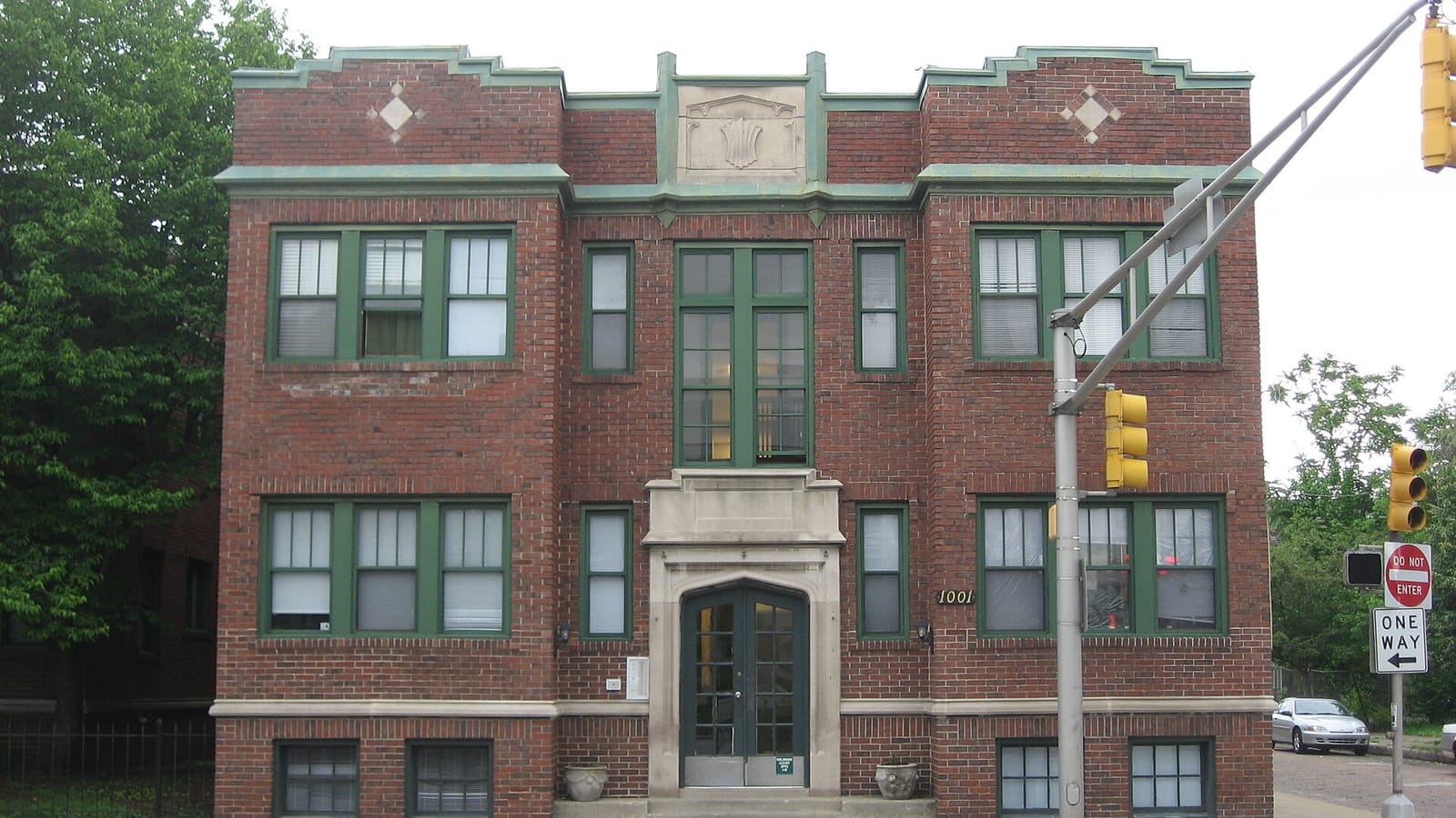 Three-story red brick apartments with green window frames and a stone entrance