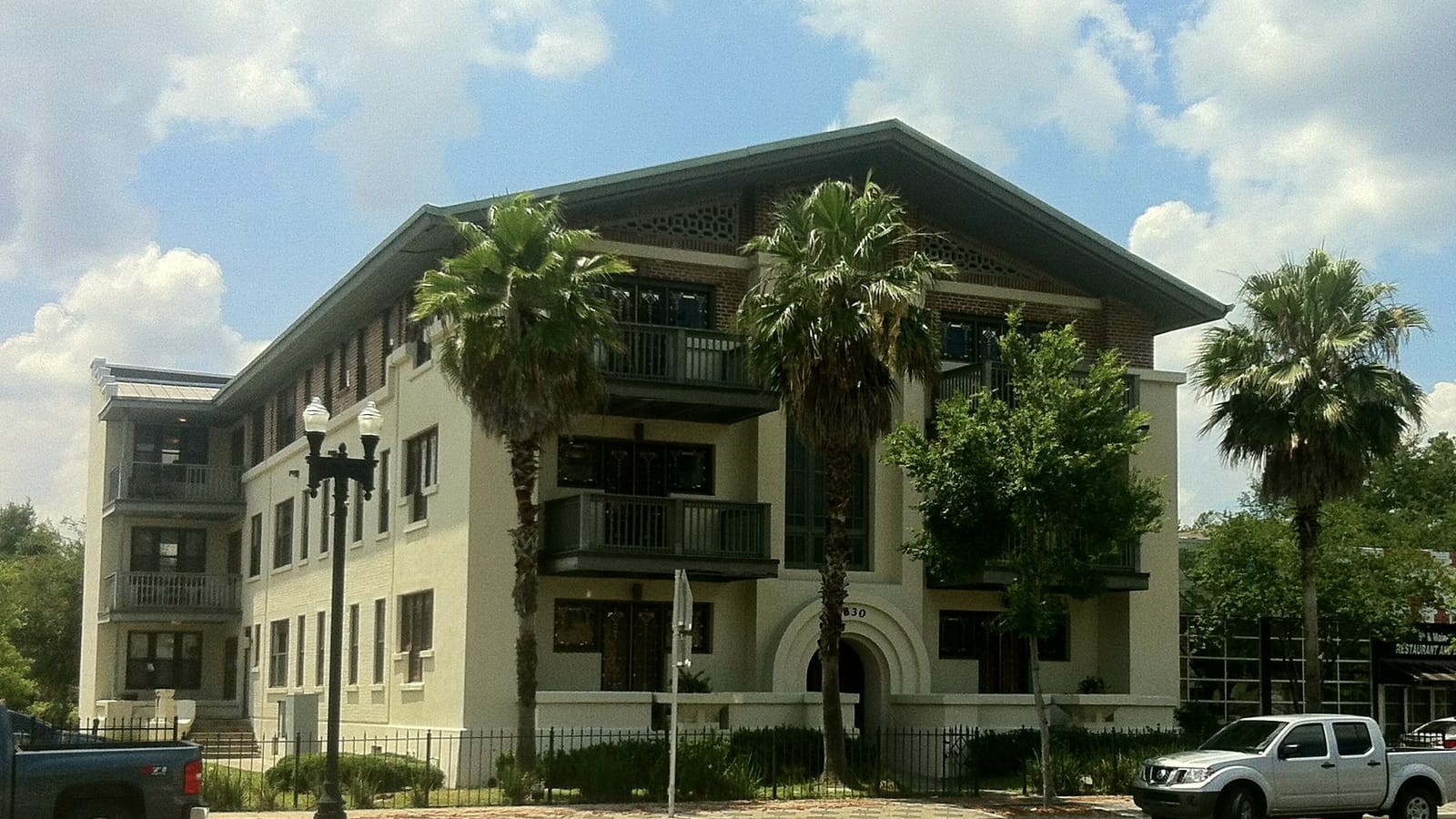 Pale apartment building with deep balconies and palms along the sidewalk