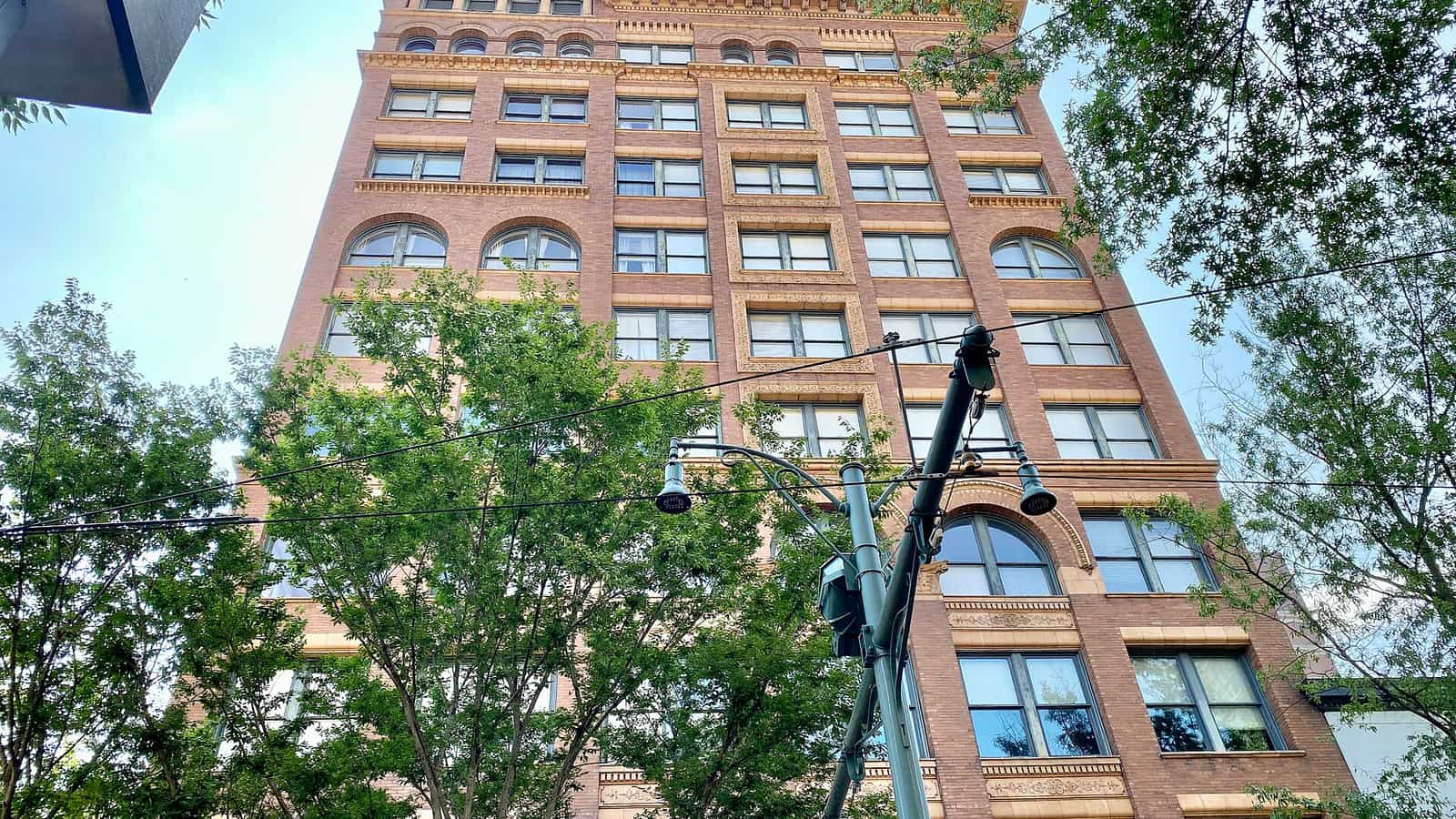Tall brick facade with paired windows and decorative arched openings behind street trees