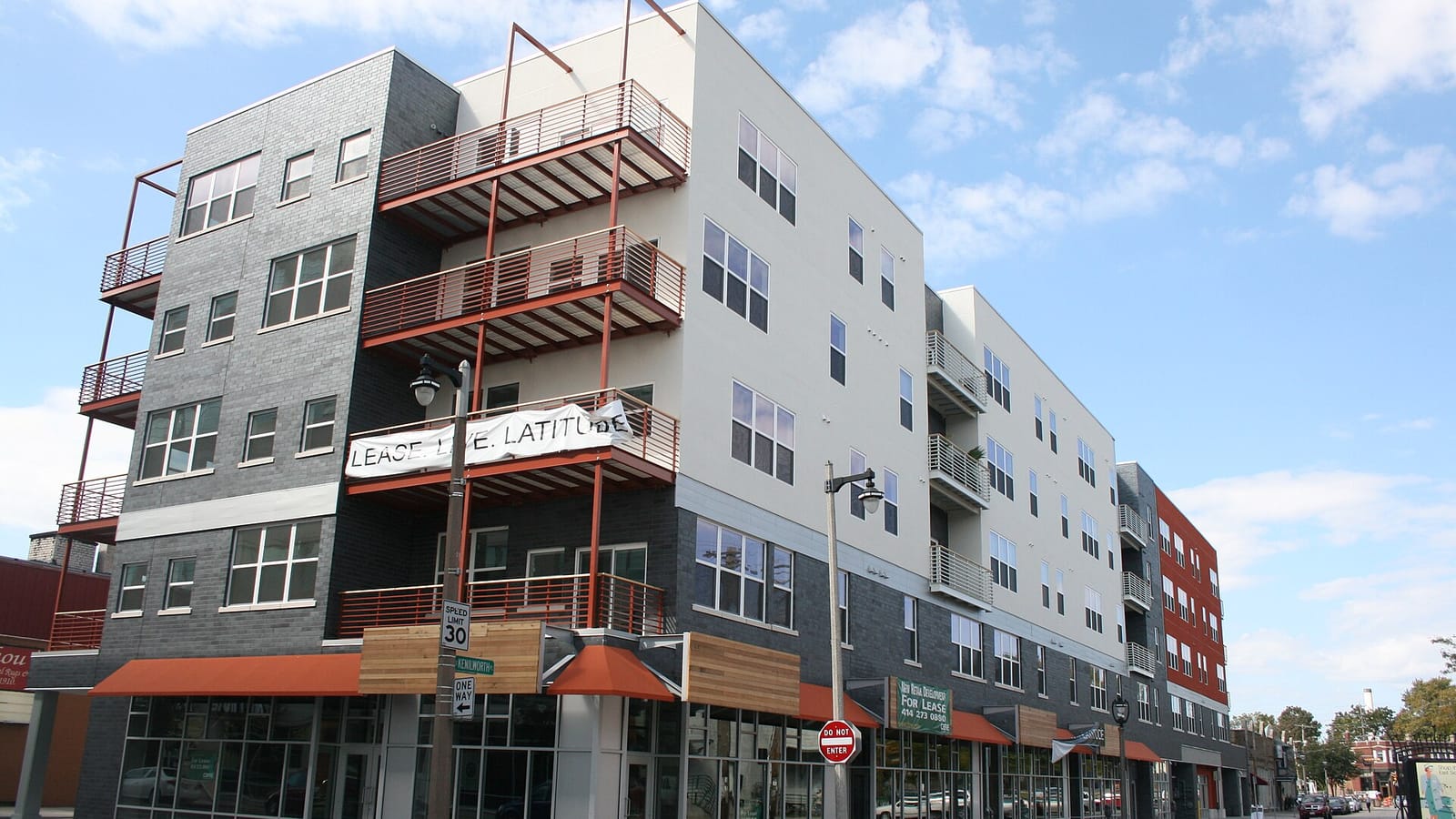 Modern gray apartment building with red-framed balconies and a wood-clad entrance