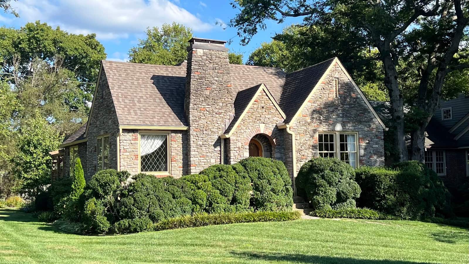 Stone house with steep gables and shrubs beside a lawn