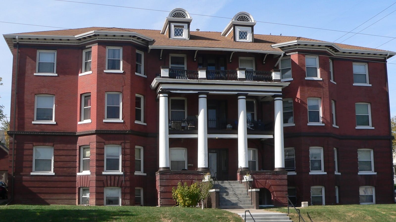 Front facade of a red brick apartment building with deep columned balconies