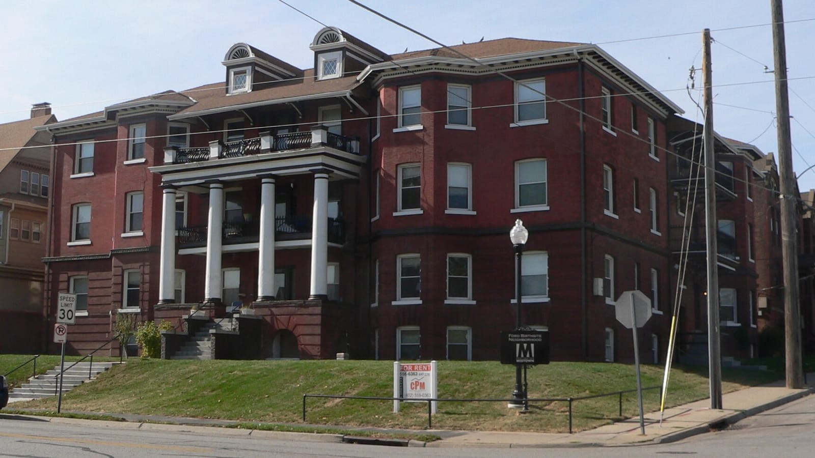 Red brick apartment building with a columned entrance and small front lawn