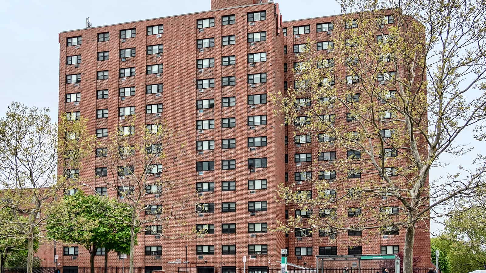 Tall rectangular red brick apartment building behind leafing street trees