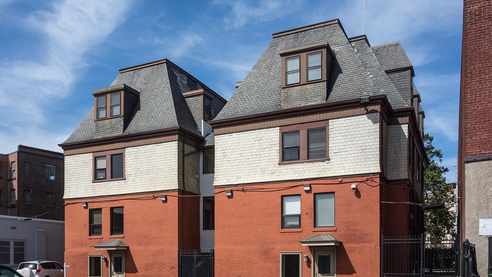Pair of older apartments with red brick lower floors and steep gray roof sections