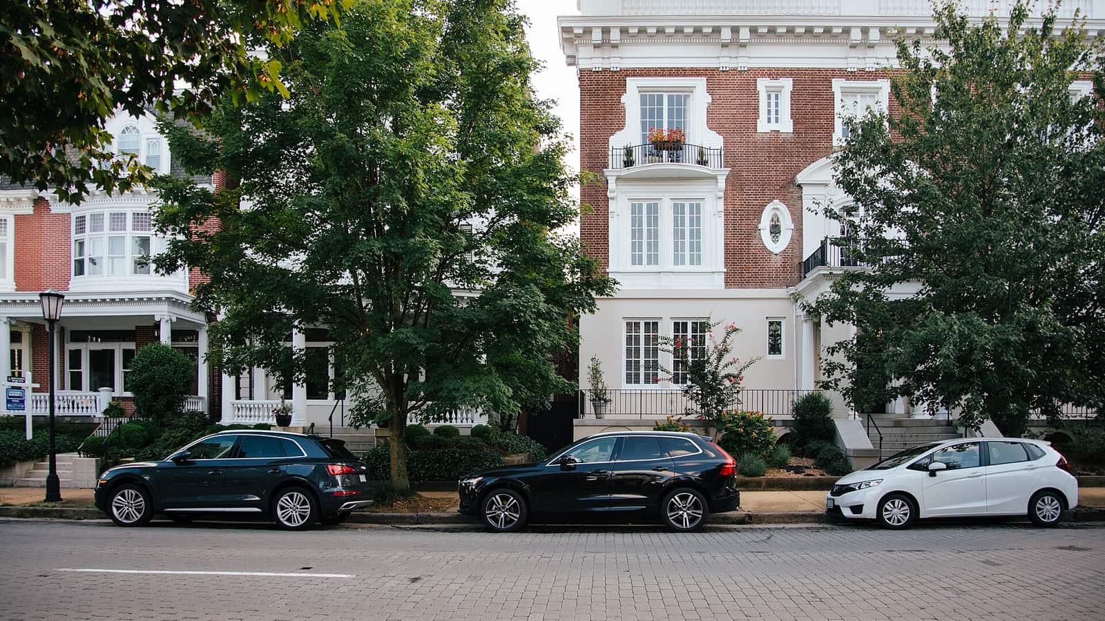Red brick apartment facades with white trim and balconies above a tree-lined sidewalk