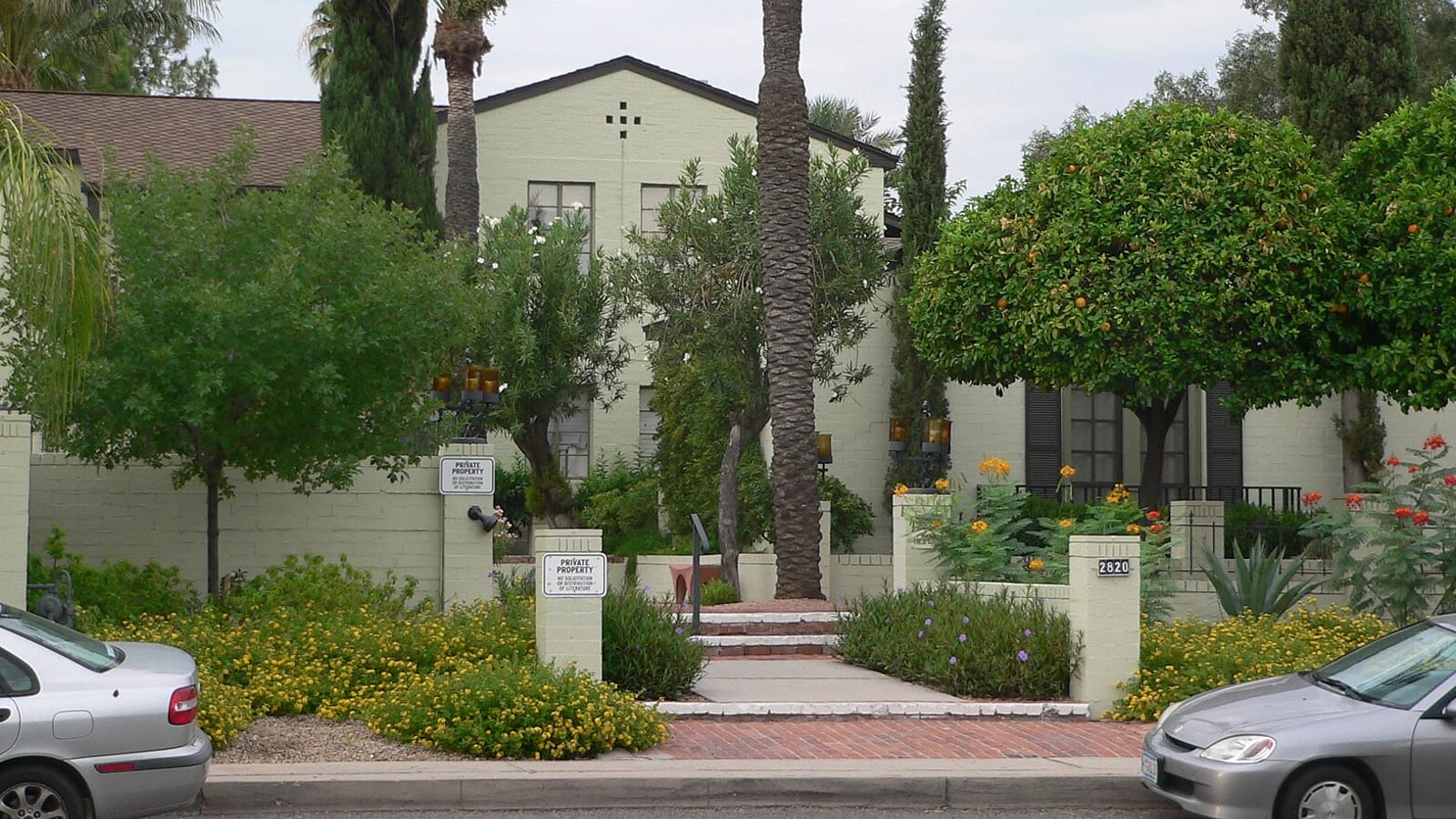 Pale stucco apartment building with a central entrance and tall narrow trees