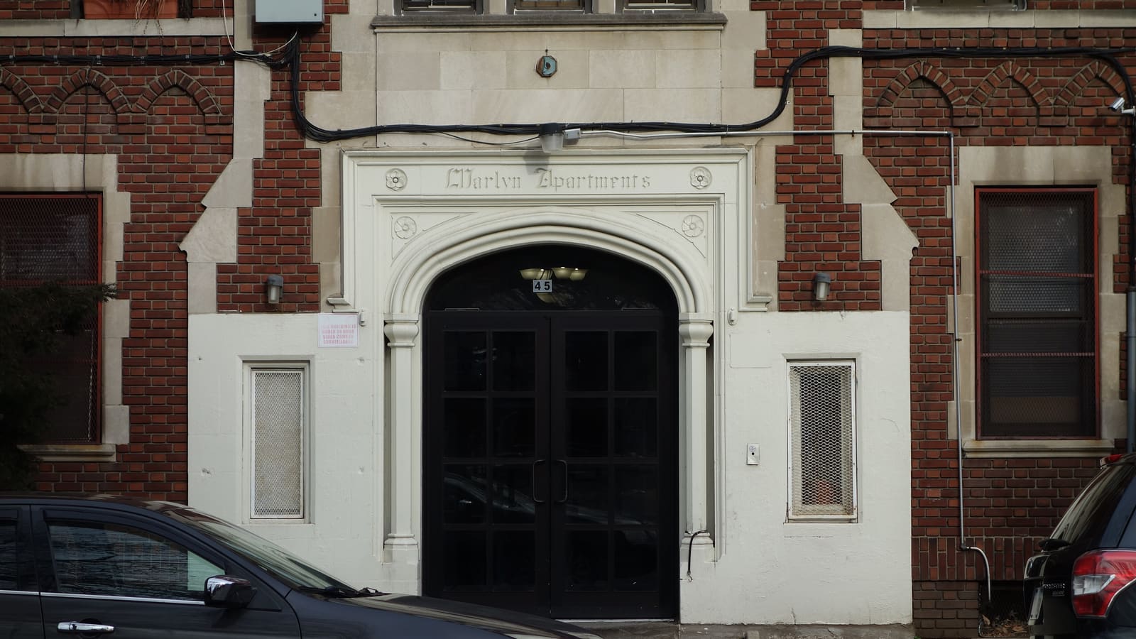 The arched stone entrance of a red brick apartment building, numbered 45, with black double doors and the building name carved above.