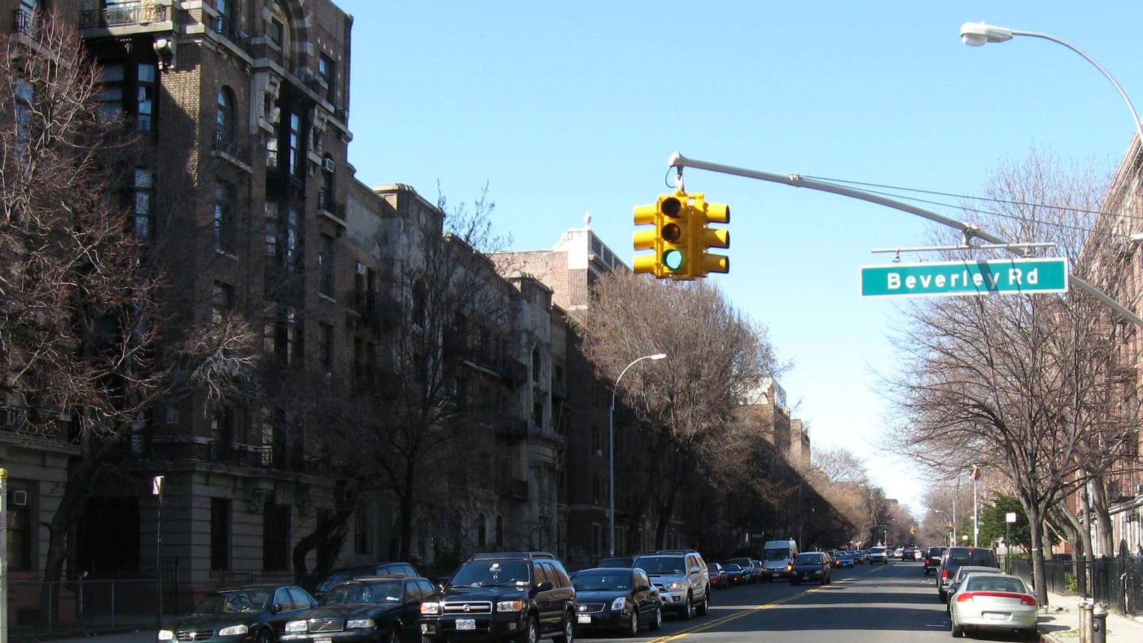 A street lined with brick apartment houses and parked cars under a Beverley Road street sign