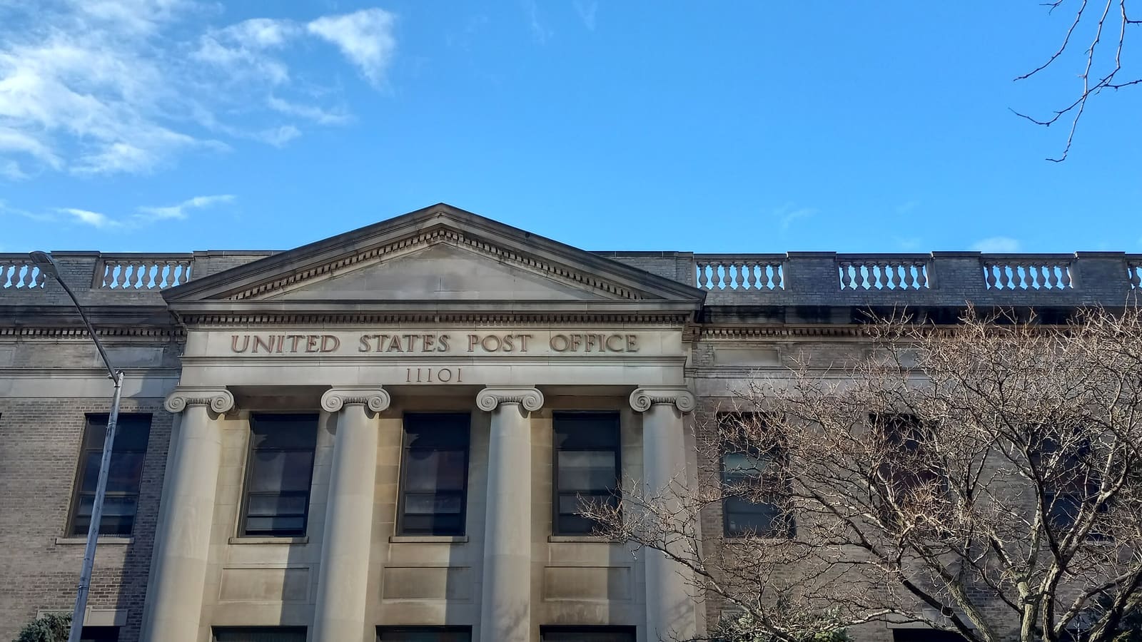 The stone front of a post office under a blue sky, with four columns below a pediment carved United States Post Office and the ZIP code 11101.
